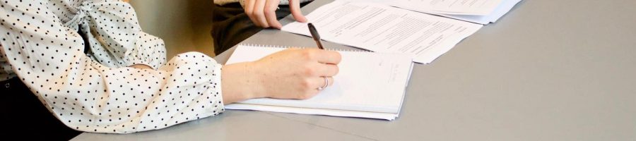 woman signing on white printer paper beside woman about to touch the documents